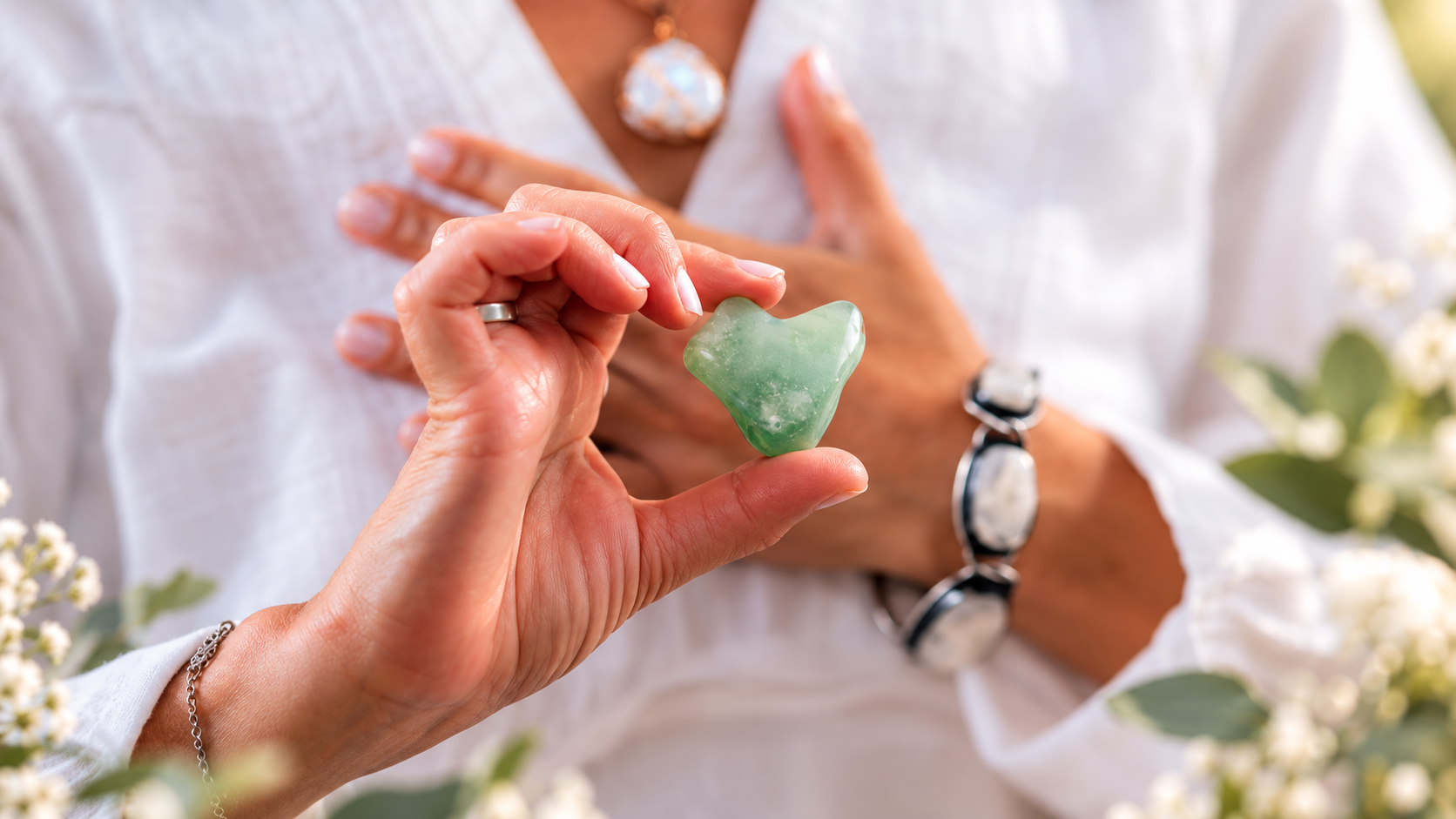 Ruka drží zelený avanturín ve tvaru srdce, v pozadí žena v bílém.